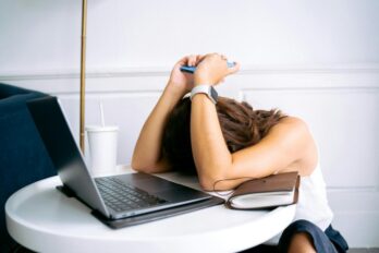 Devojka spuštene glave na sto pored laptopa