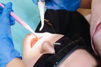 Zubarka radi zub pacijentu instrumentima.