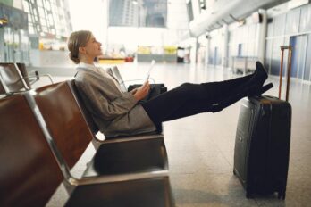 žena sedi u čekaonici na aeorodromu sa podignutim nogama na koferu