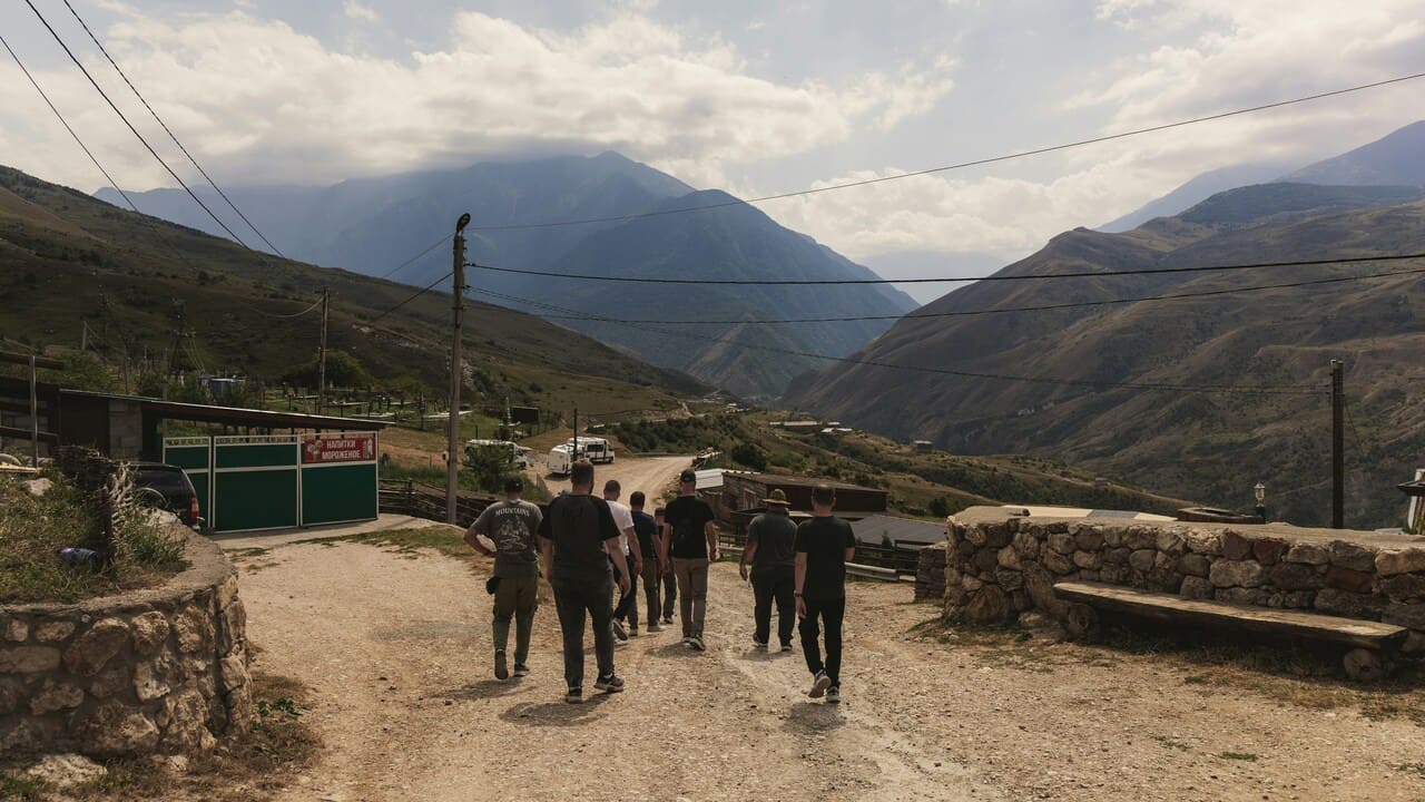 Grupa ljudi šeta makadamskim putem kroz planinsko selo u podnožju planina