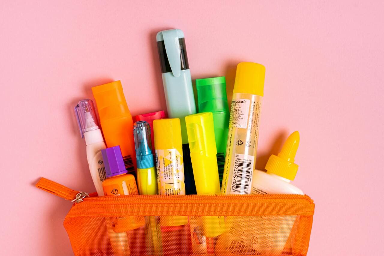 Narandžasta pernica puna šarenih markera i lepka na roze podlozi