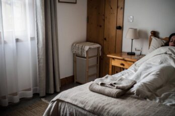 Žena zavaljena u krevetu pokrivena belim ćebetom u prigušenoj spavaćoj sobi